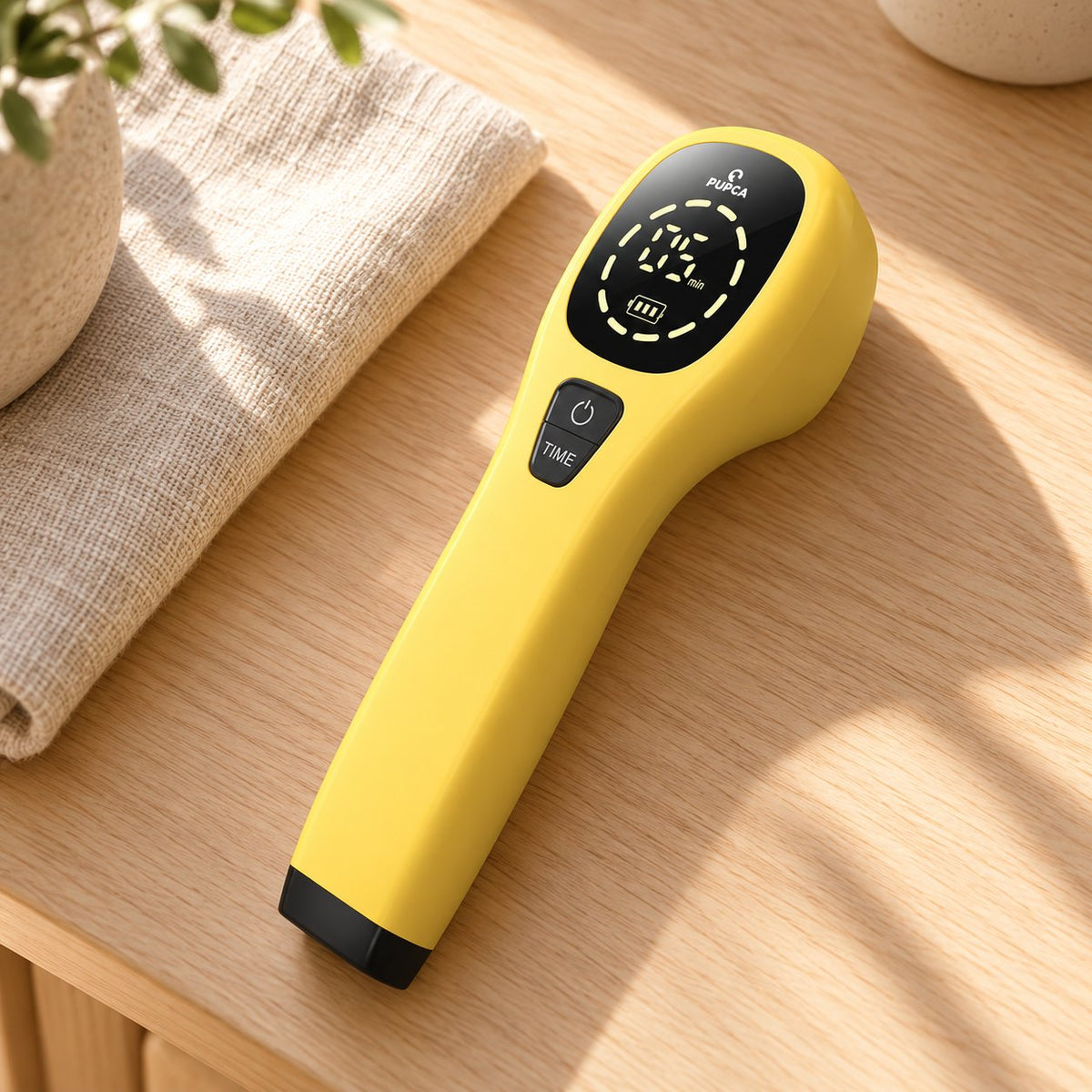 PUPCA handheld red-light device resting on a pale wooden table beside a folded cloth.