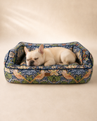 Cream French Bulldog sleeping in a Morris & Co Strawberry Thief pet sofa bed on a warm neutral background
